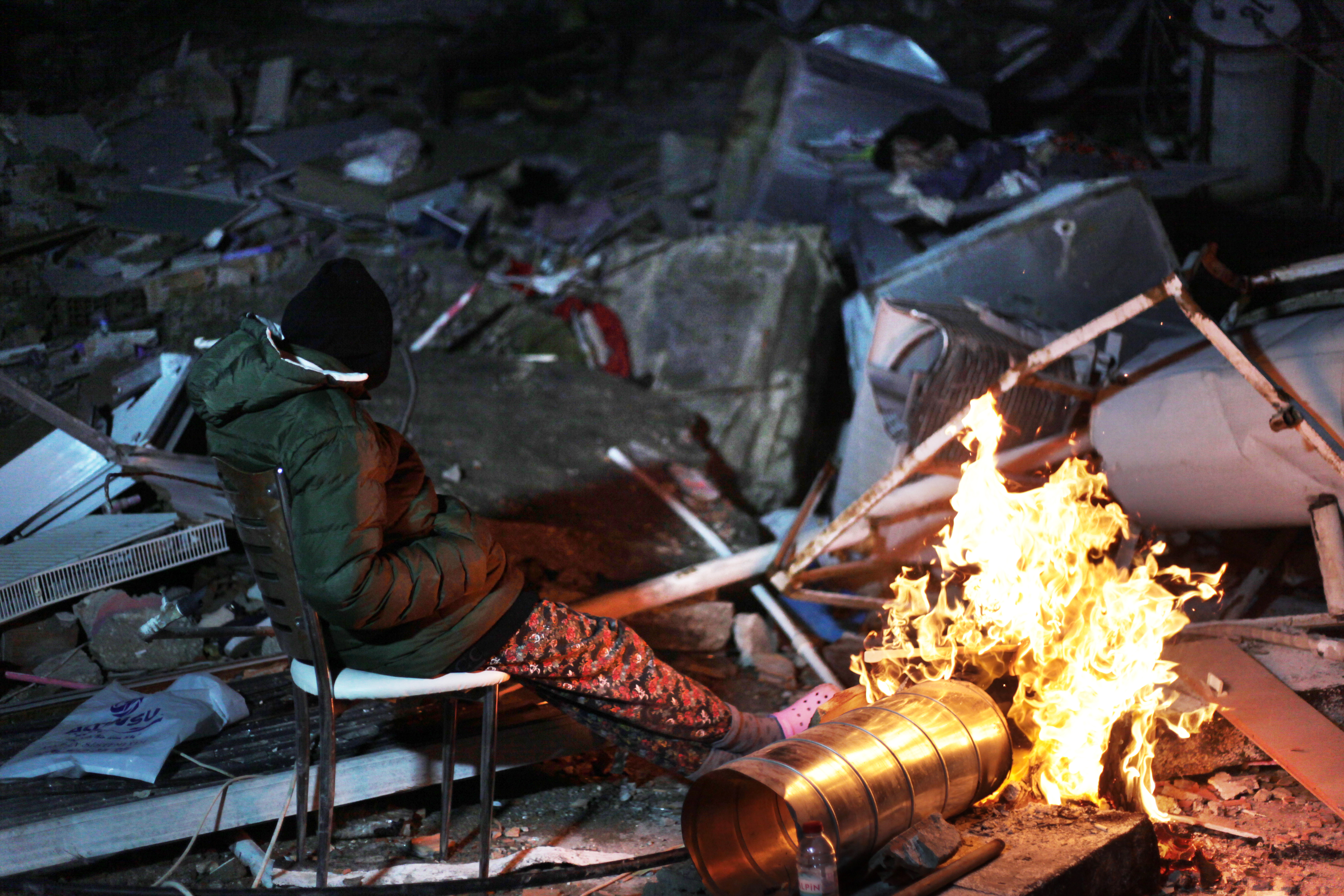 A survivor of the earthquakes warms up by the fire in Hatay. Photo: Özge Ergin.