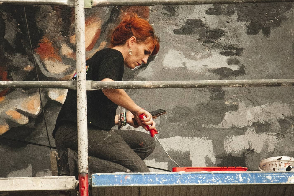 Artist Lebibe Topalli in the process of painting her mural “What you sow, you reap” in the municipality of Ferizaj, Kosovo. Photo: Donit Avdyli / Mural Fest
